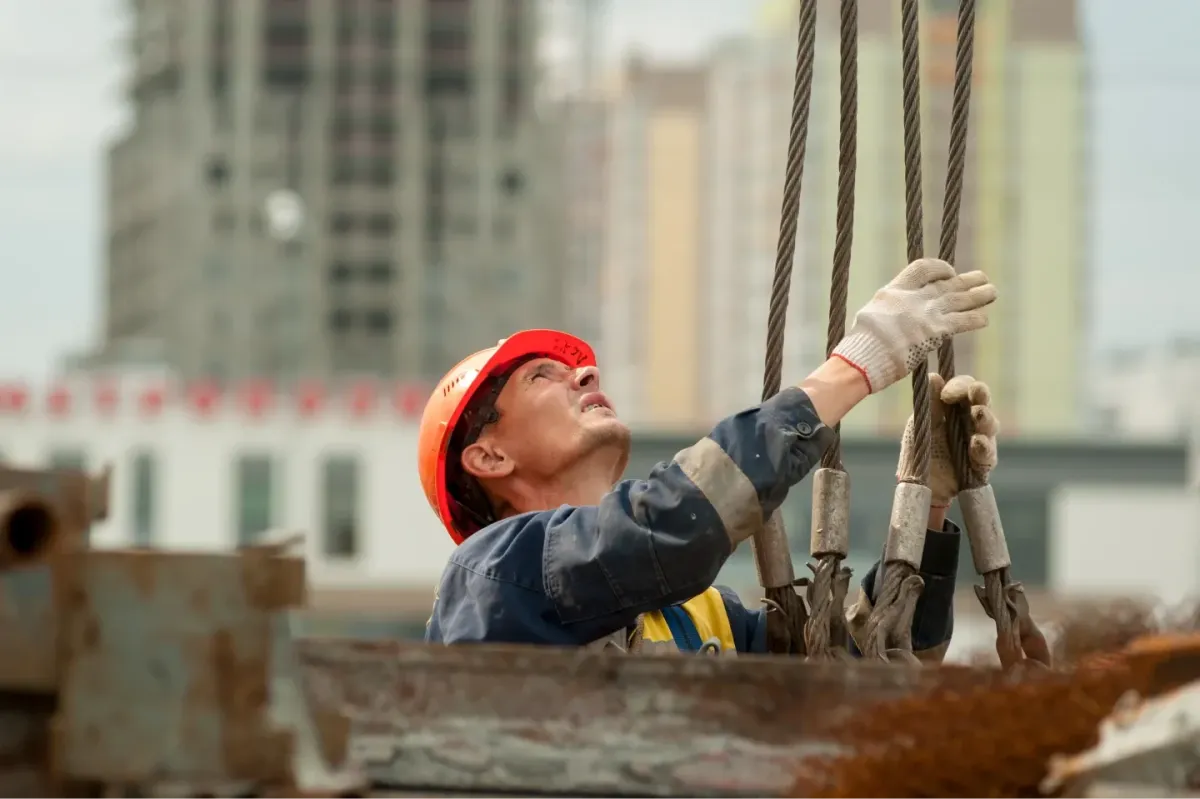 Construction worker in a hard hat guiding lifting slings and rigging equipment on a job site