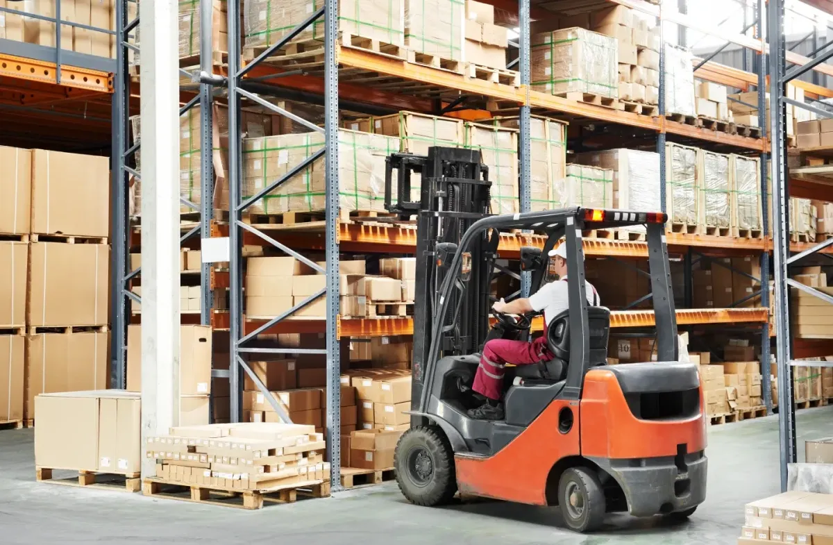 Forklift operator moving pallets inside a large warehouse with high storage racking