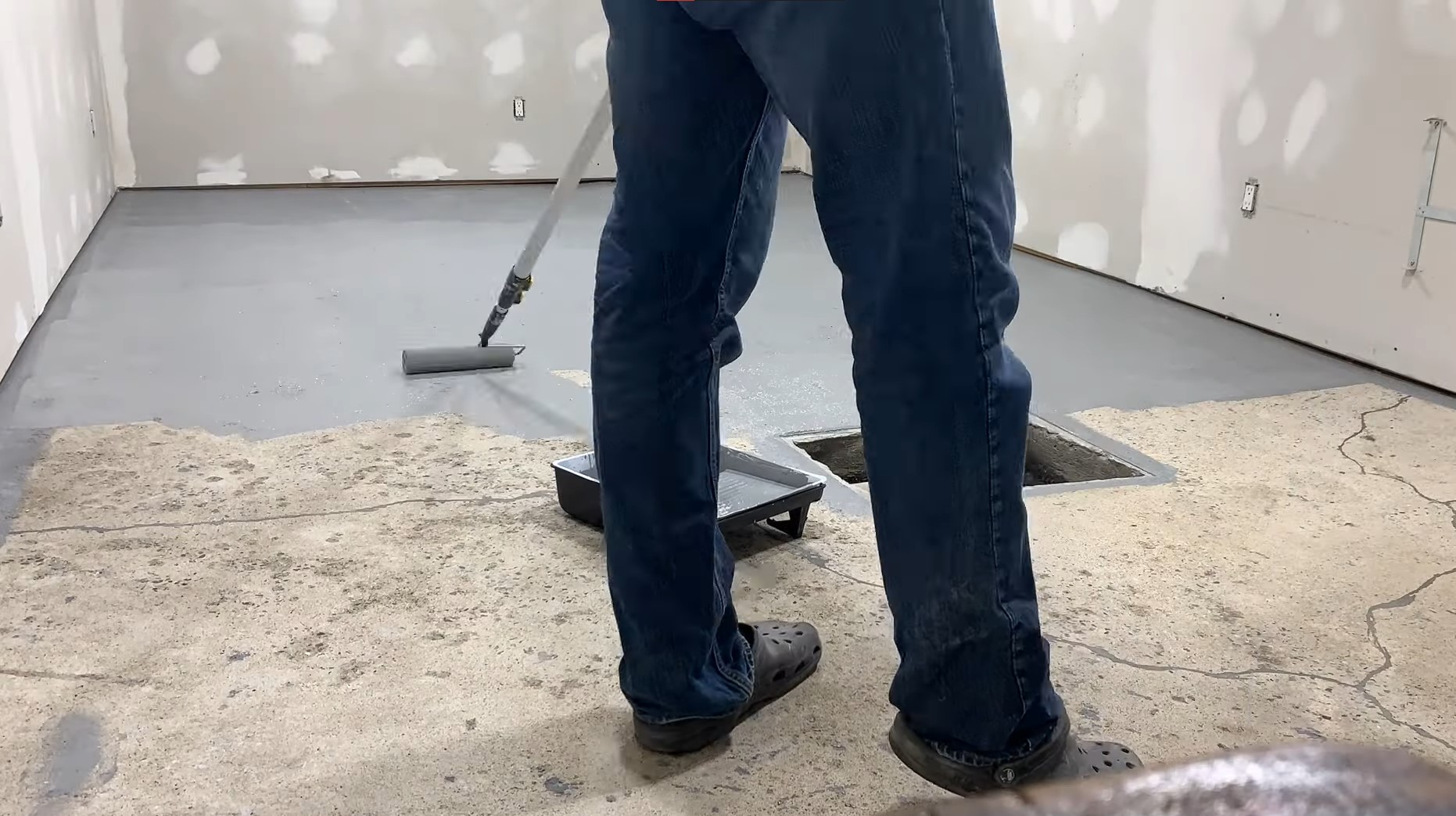 man using roller to roll grey epoxy floor over concrete floor