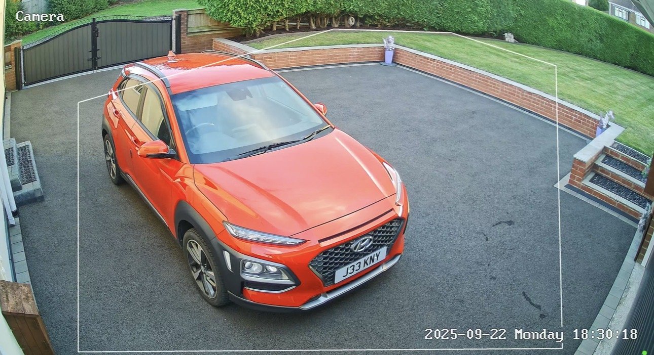 CCTV camera view of a large tarmac driveway with an orange car and gated entrance, installed by L&B Security