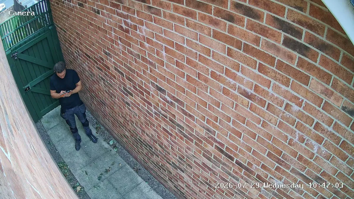 CCTV camera view down a narrow brick side passage towards a green gate