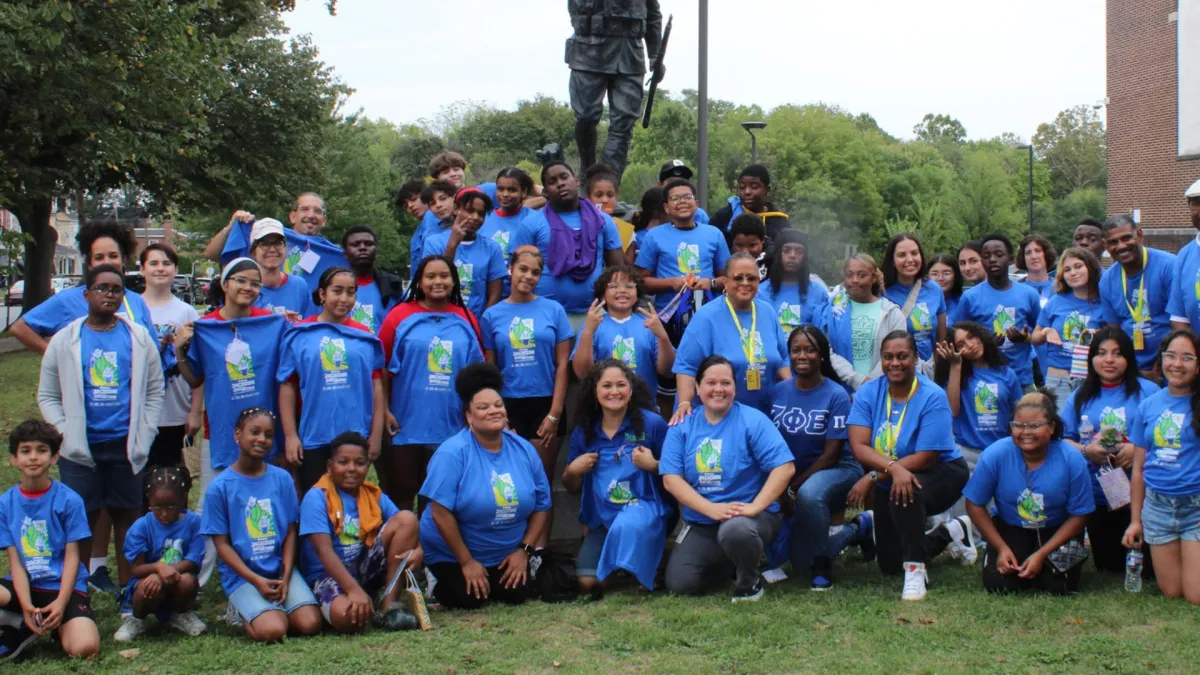 Featured program hero image of smiling students outdoors holding handmade banners and books.