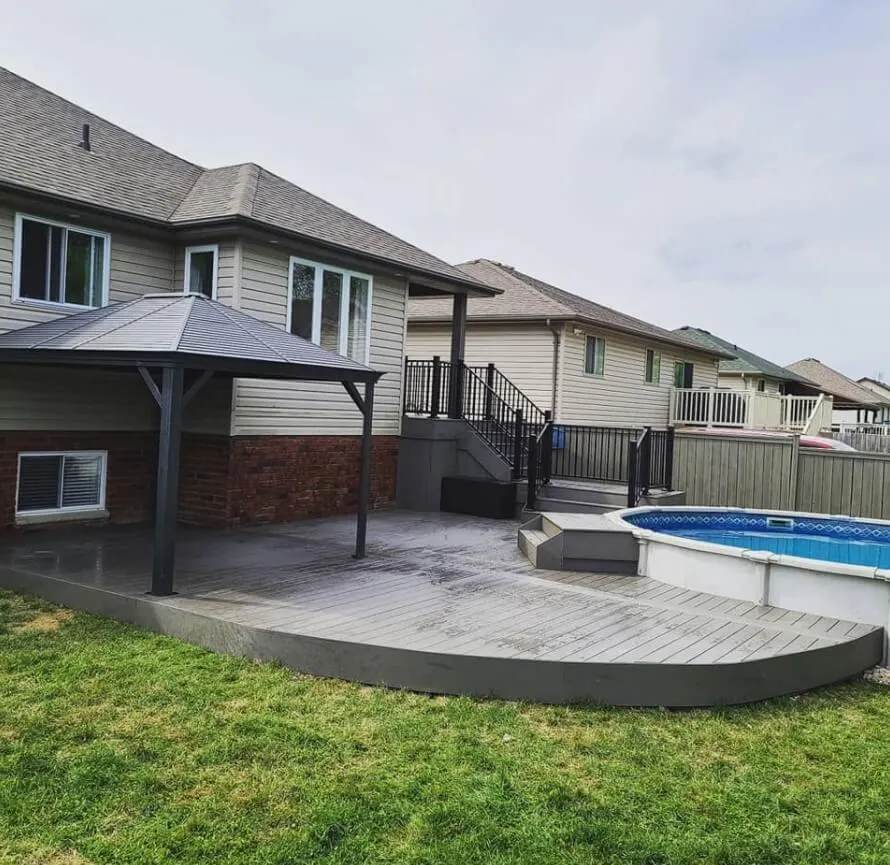 Backyard deck with a curved edge, covered gazebo, black railings, and an above-ground pool attached to a suburban house.
