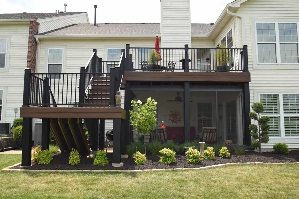 Two-story house with an elevated wooden deck featuring black railings, stairs, and a screened-in patio area below.