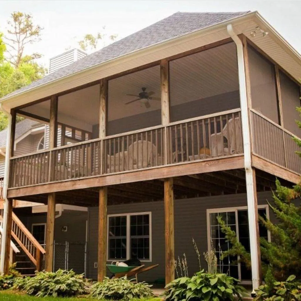 Two-story house with a raised screened-in porch featuring wooden railings, ceiling fan, and seating area.