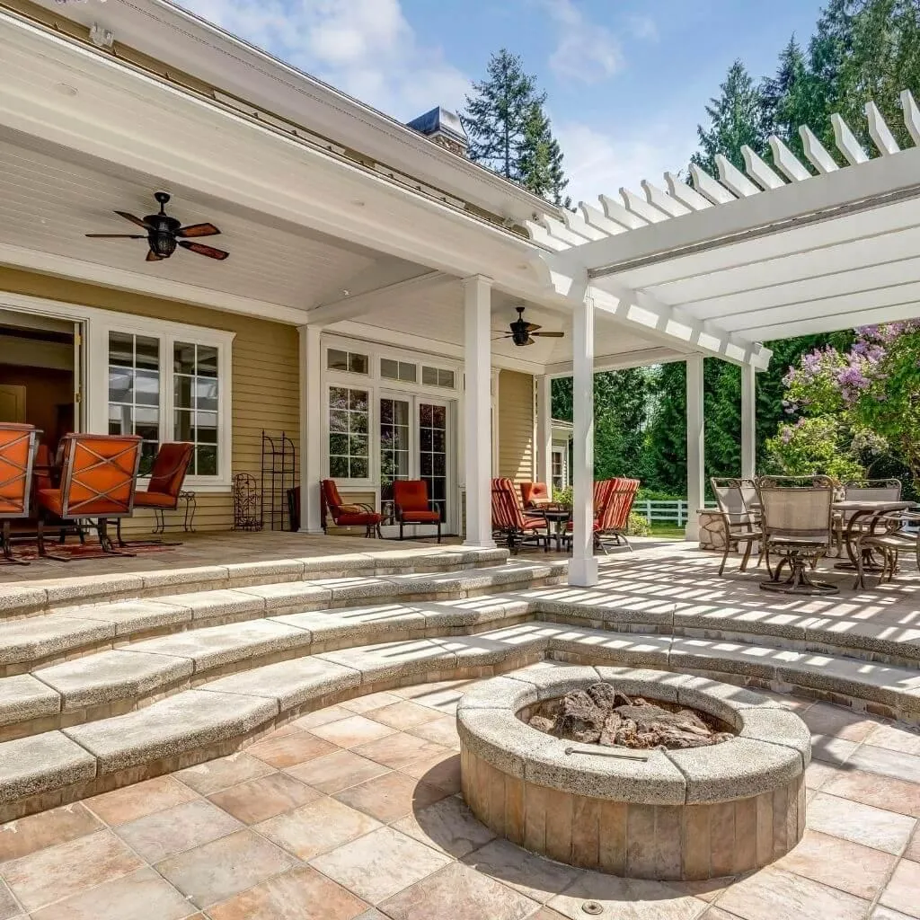 Spacious backyard patio with stone steps, fire pit, white pergola, and multiple outdoor seating areas attached to the house.