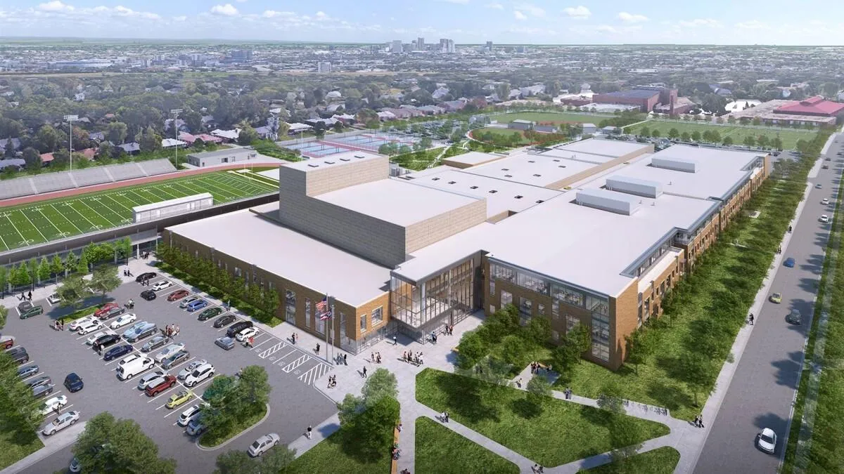 Aerial view of a large modern school campus with sports fields, parking lot, and surrounding city neighborhood