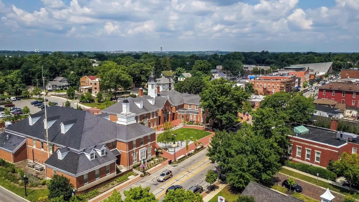 Aerial view of a small-town downtown district with historic red-brick buildings, tree-lined streets, and local shops on a sunny day