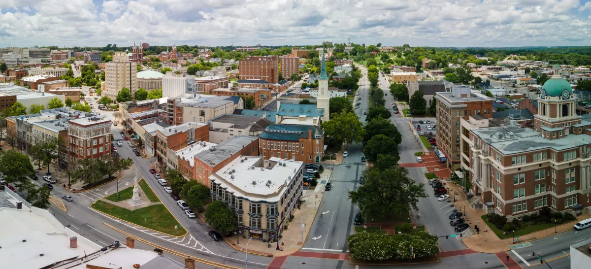 Aerial view of historic downtown with brick buildings, tree-lined streets, and city landmarks under a partly cloudy sky