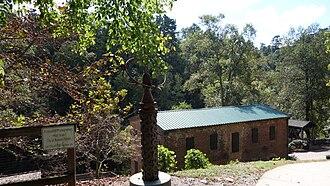 Historic brick building with green roof surrounded by trees in a wooded park setting
