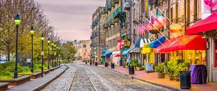 Colorful historic street with cobblestone road, shops, restaurants, and bright awnings at sunset