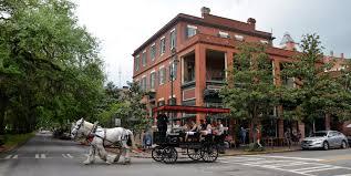 Horse-drawn carriage with tourists passing historic red-brick building on a tree-lined downtown street
