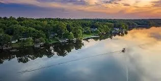 Aerial view of a lake at sunset with boats leaving ripples in the water and houses along the wooded shoreline