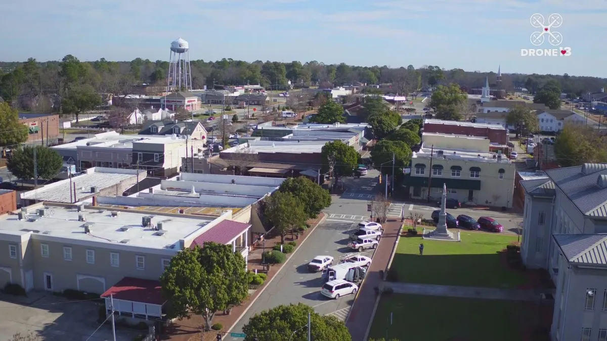 Aerial view of small-town downtown with low-rise buildings, water tower, and cars parked along the main street