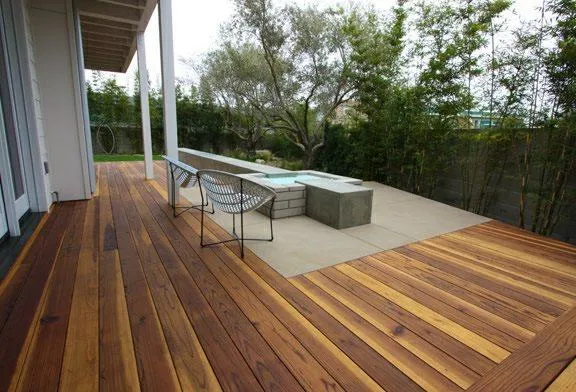 Modern backyard deck with rich wooden flooring, two chairs, and a built-in rectangular concrete water feature.