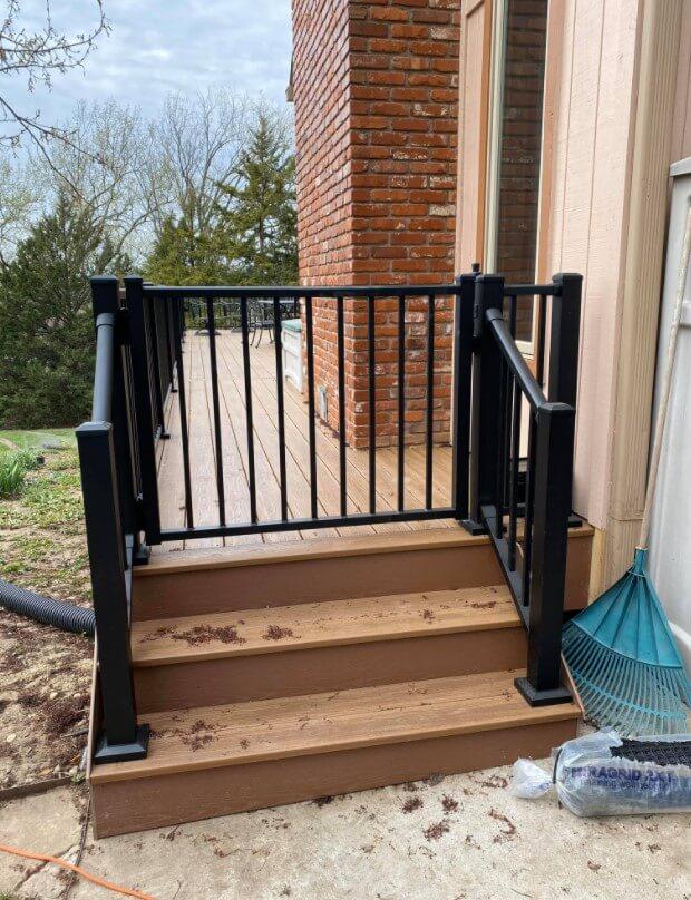 Small wooden deck staircase with black metal railings, leading to a brick house exterior and sliding glass door