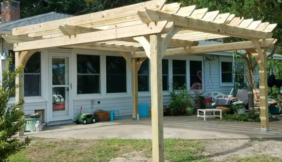 Backyard patio with a newly built wooden pergola attached to a single-story house, surrounded by outdoor seating and toys.