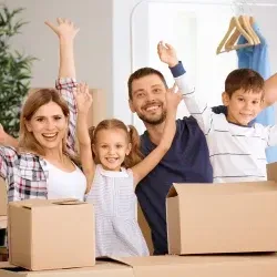 Šťastná rodina se usmívá a mává obklopená krabicemi během stěhování se společností STĚHUJEME PRAHU.