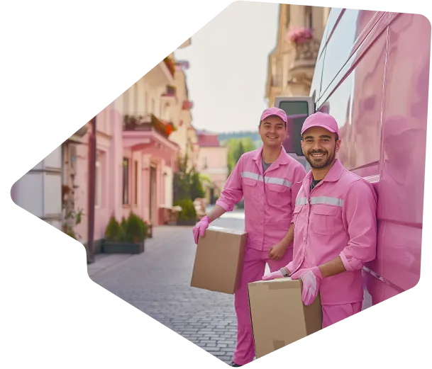 Dvaja usmievaví sťahováci v bielych tričkách a fialových montérkach nesú veľkú krabicu zabalenú v plastovej fólii. Sťahováci sa nachádzajú v modernom, svetlom obývacom priestore s veľkými oknami, cez ktoré preniká prirodzené svetlo. V pozadí je niekoľko zabalených krabíc a biely gauč. Vonku cez okná je vidieť zelenú krajinu.