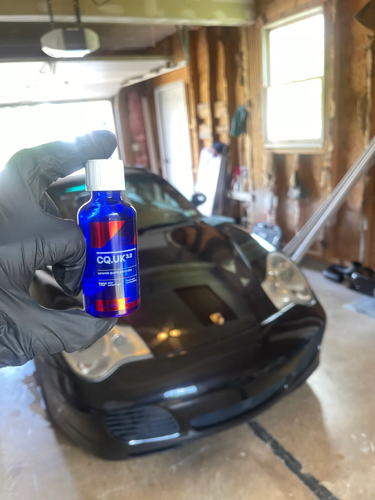 A black Porsche Carrera with a bottle of  carPro Quartz 3.0