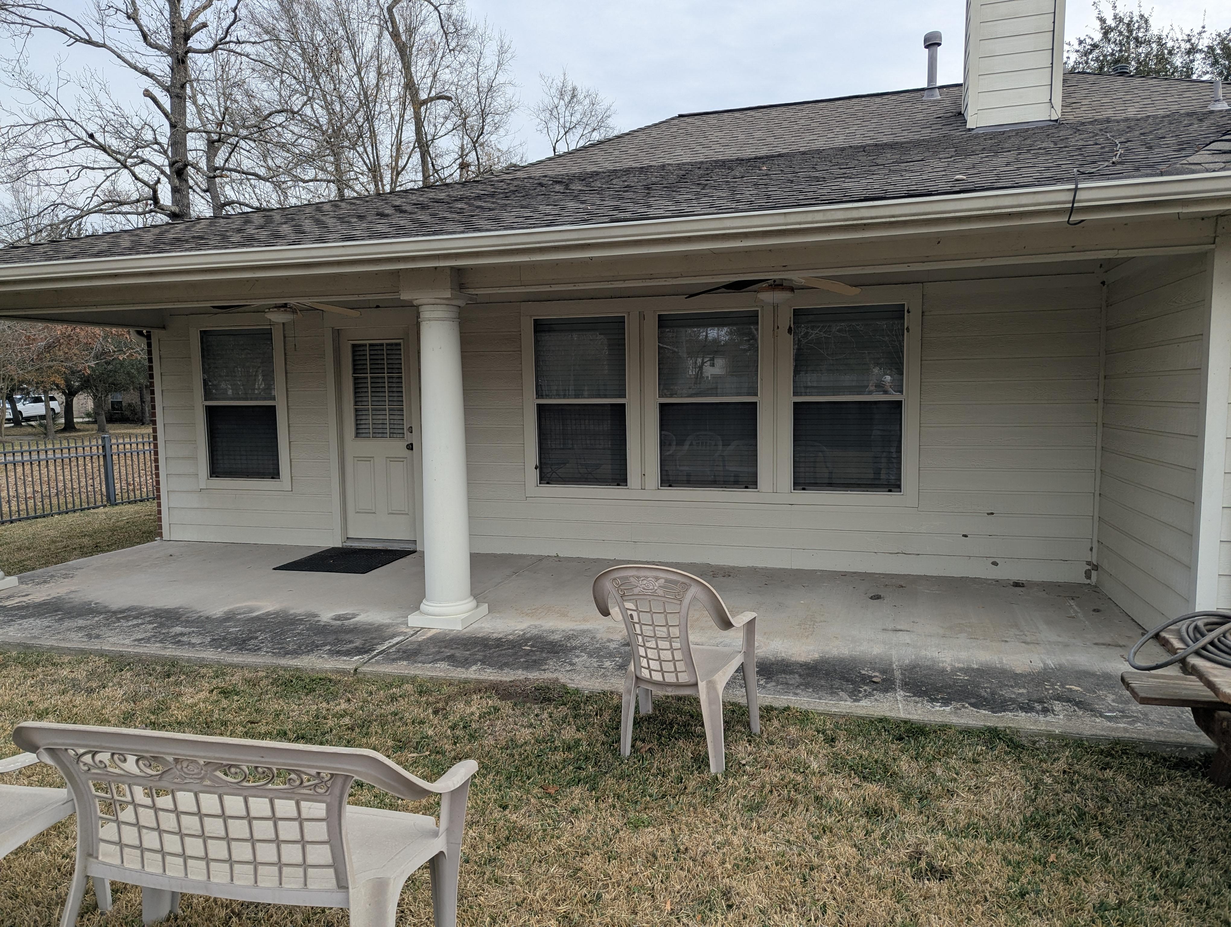 Back patio and concrete slab before pressure washing in Houston TX with dirt, mildew, and algae buildup on siding and porch surfaces