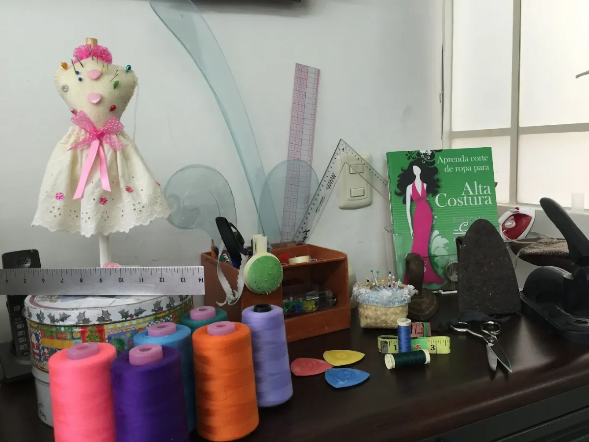 Mesa de trabajo de una modista con materiales básicos de costura, hilos de poliéster, reglas técnicas y el manual de Alta Costura de Sistema CyC para el diseño de prendas a medida