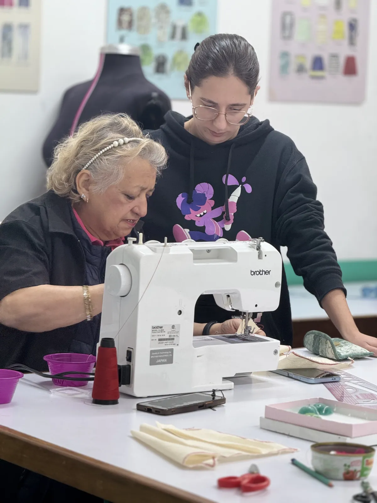 Una estudiante sonriente de la Academia CyC posa con orgullo junto a un maniquí que viste una pijama azul claro con vivos blancos, confeccionada por ella misma. La fotografía está tomada en un taller de costura real donde se aprecia el logotipo de "Sistema CyC desde 1935", burros de planchar y carteles educativos sobre el método de corte y confección. La imagen captura el espíritu de "aprender haciendo" y la satisfacción de alcanzar la autosuficiencia mediante la creación de prendas propias