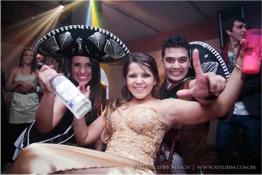 Convidada de vestido dourado posa com integrantes da equipe usando sombreros