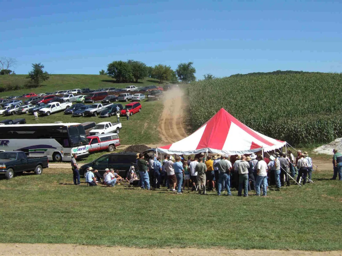 Farm tour gathering under red and white tent near cornfield at Eric Hagan’s farm – soil health education and agroforestry workshop during 2025 field day