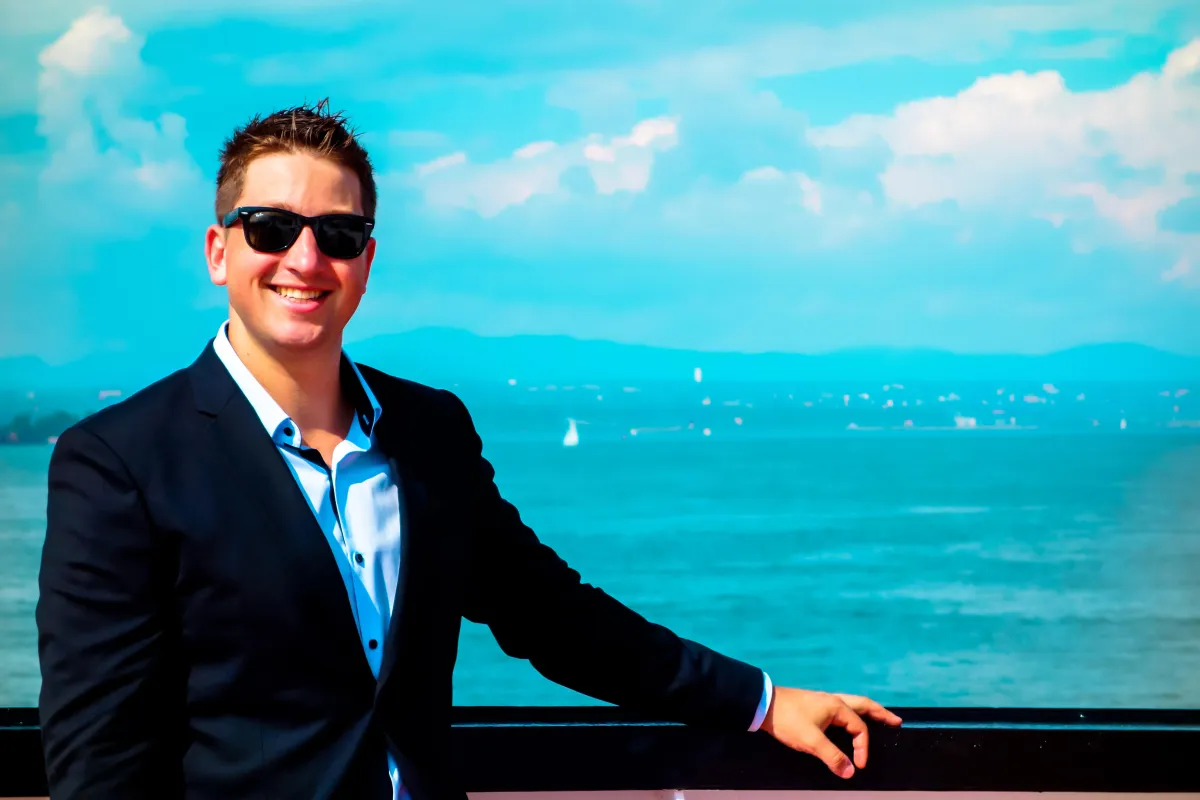 A portrait of a creative director with expressive features, wearing stylish glasses and a casual blazer, standing against a softly lit backdrop. The image conveys confidence, creativity, and approachability, highlighting leadership in media production.