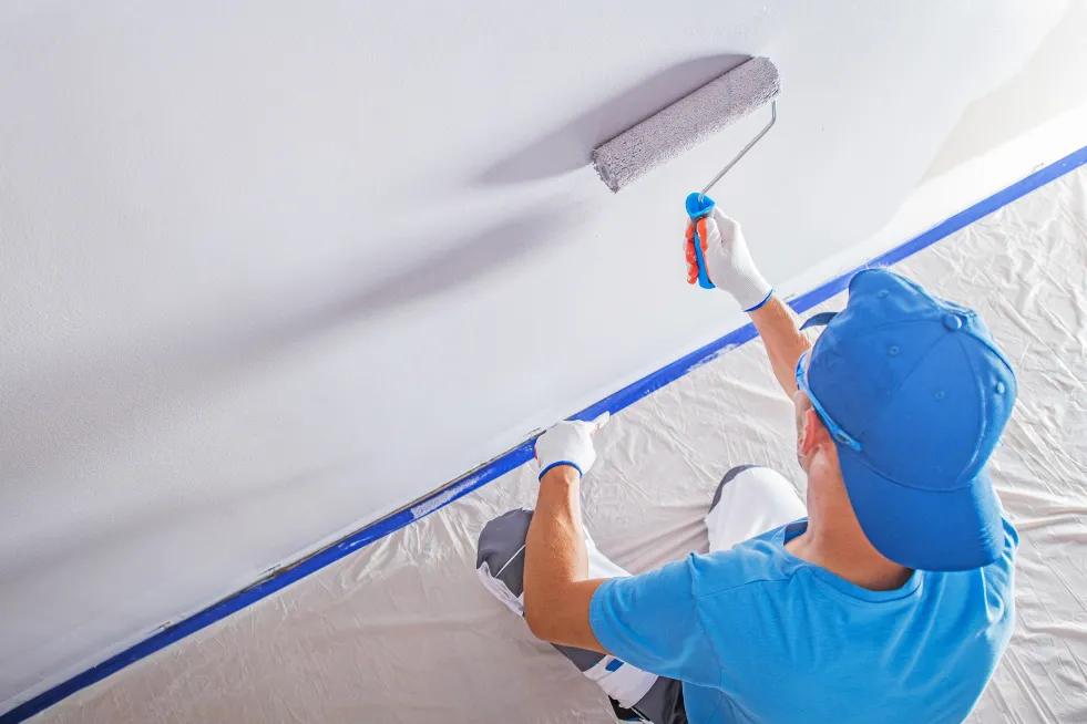 A young man using a paint roller and painting a wall white.