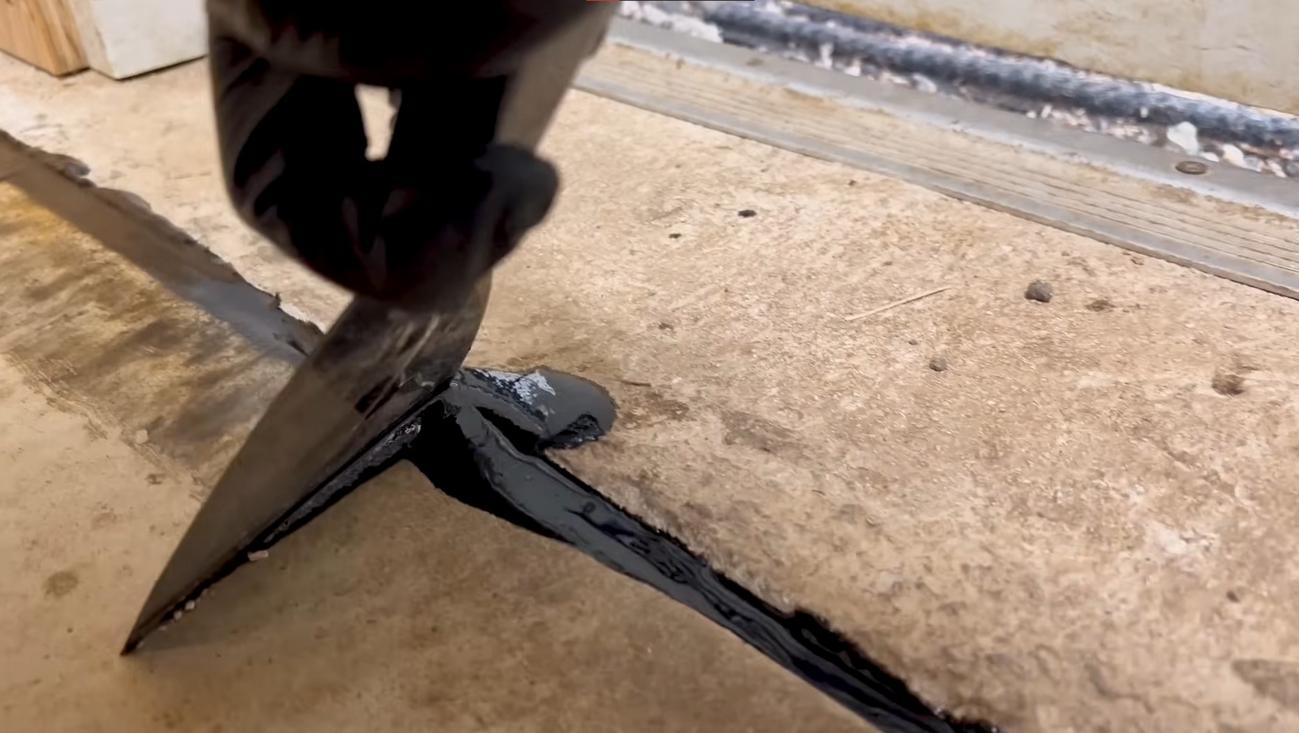 trowel being used to spread black gap filler on concrete