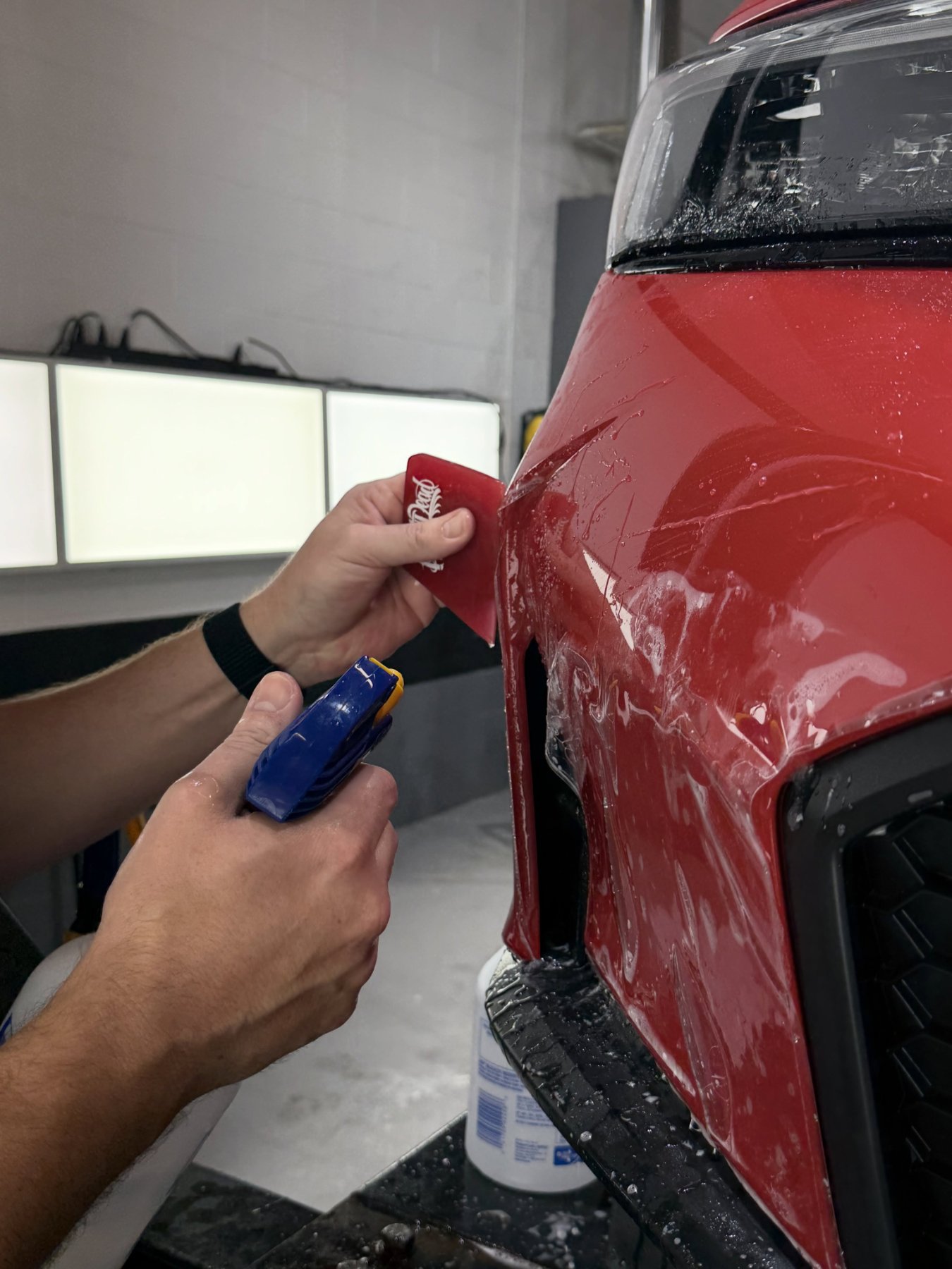 Squeegeeing paint protection film onto a red fender
