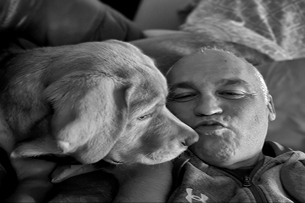 Black and white photo of Brad Walsh, host of Empowerography, sharing a tender moment with his Red Fox Labrador Memphis — an unguarded, intimate image representing vulnerability, connection, and the importance of men's mental health.