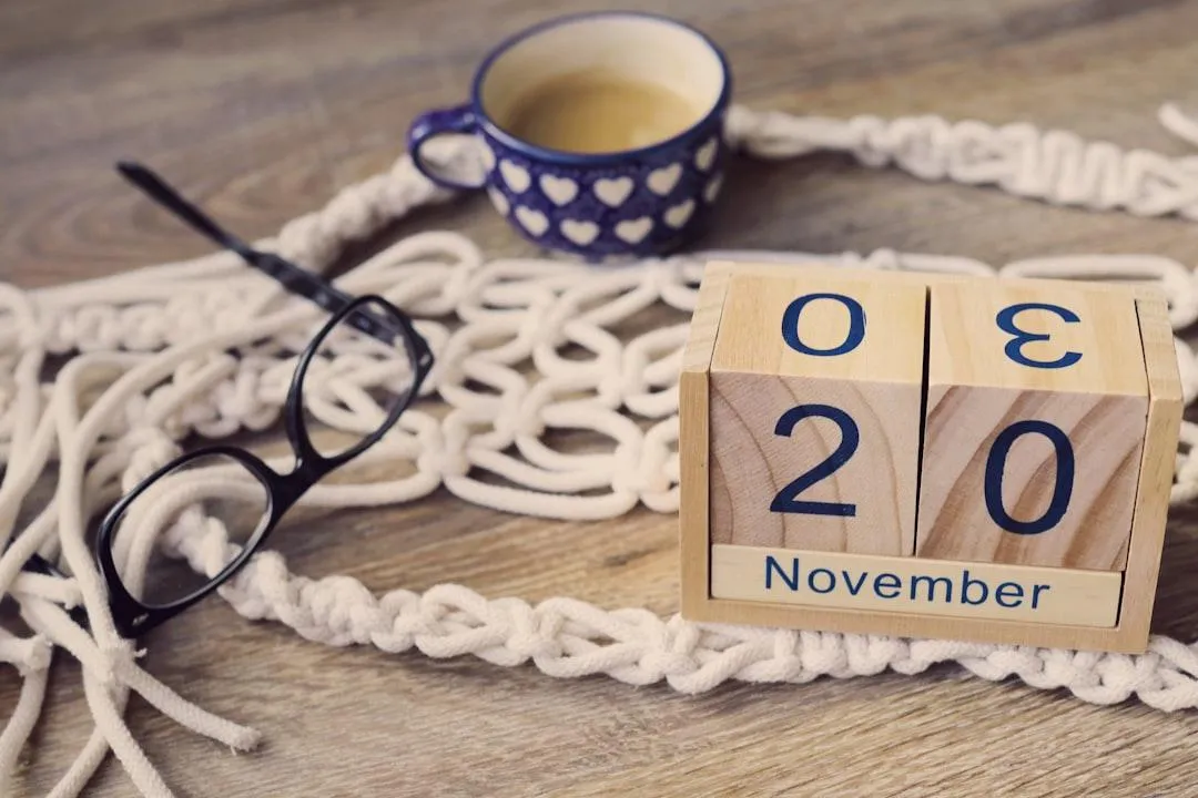 glasses lying on a piece of what looks like rope with a calendar made out of wooden blocks and a cup of tea in a blue mug with white hearts on it