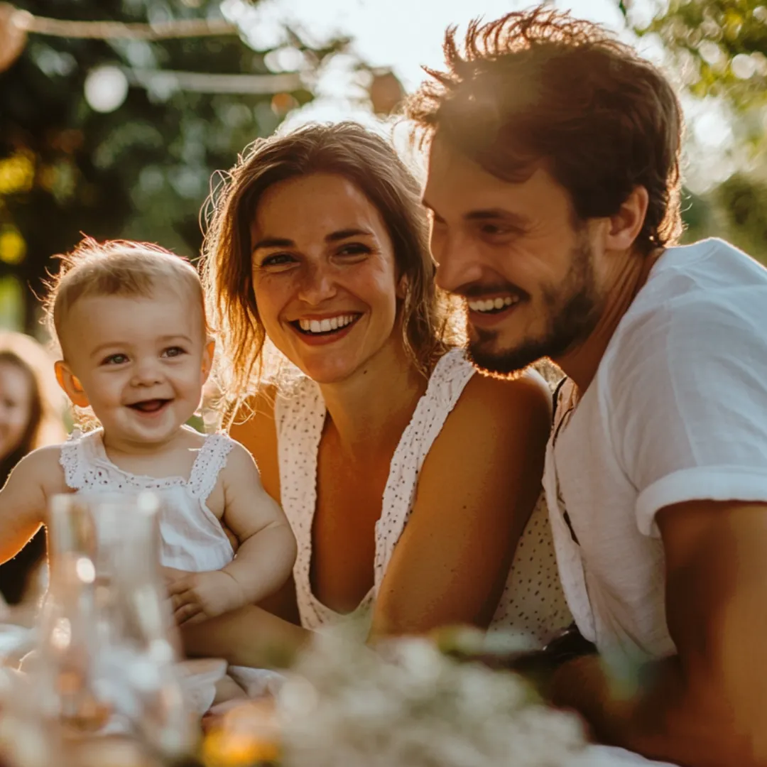 Happy parents hold their baby while sitting at an outdoor party. 