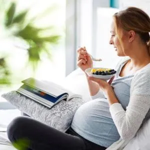 A pregnant woman relaxes in an arm chair while her dog lays at her feet.