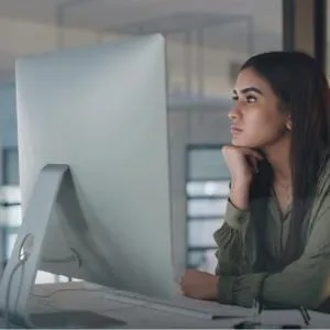 A woman sitting at her desk scrolling through her baby registry on her i-mac computer