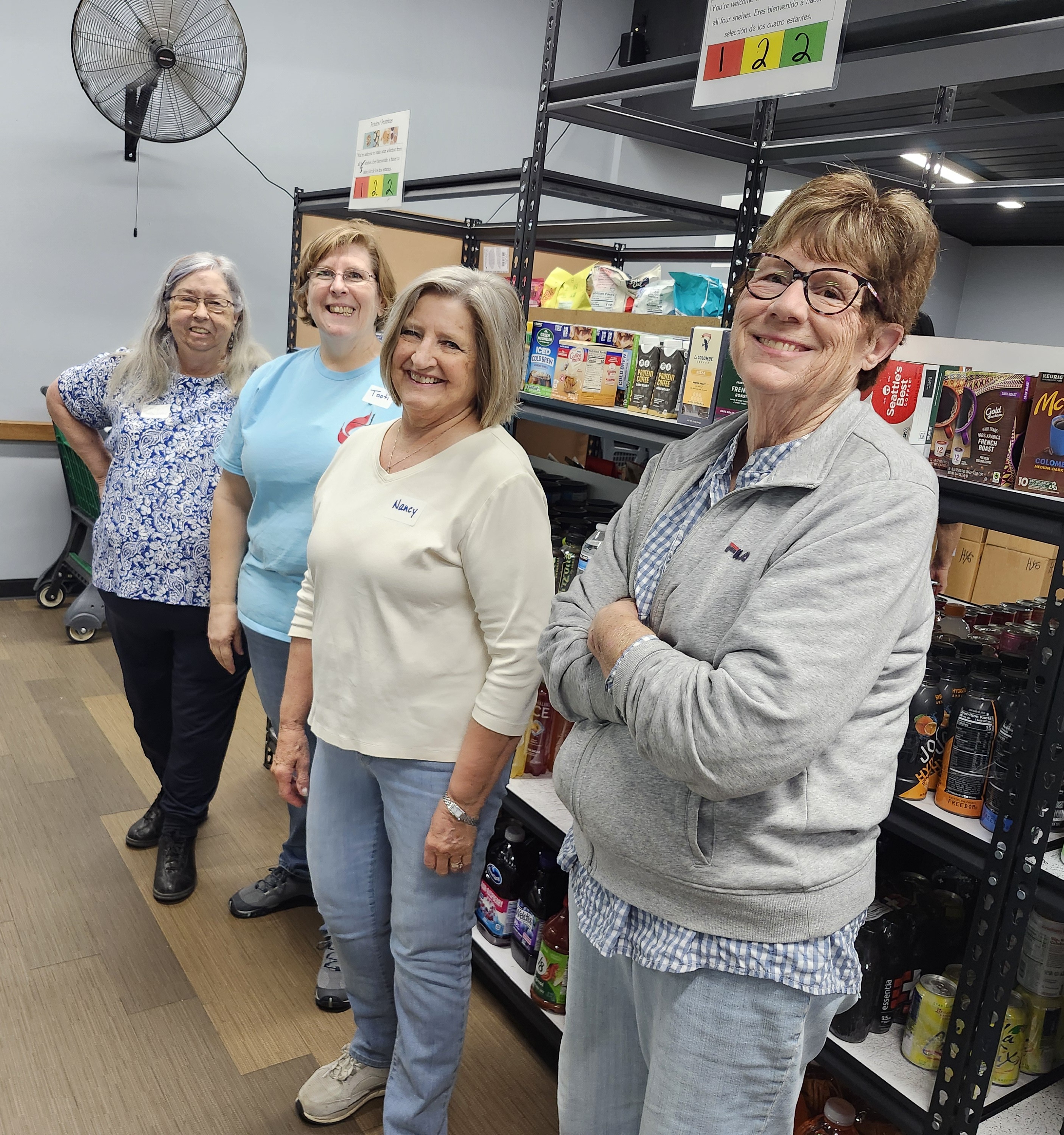 Four women smiling in a well-stocked food pantry.