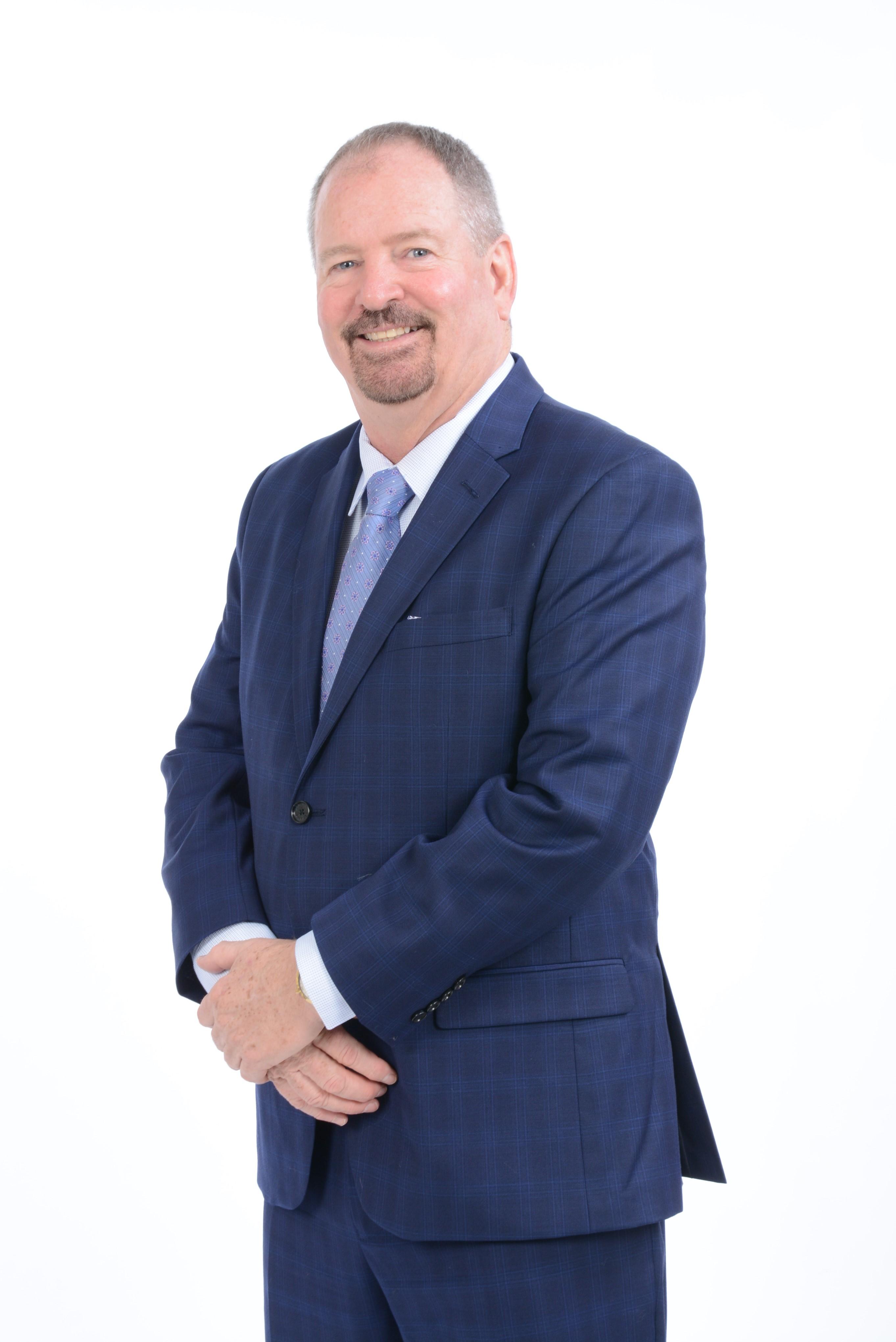 Portrait photo of a smiling middle-aged man with a goatee, wearing a blue patterned suit jacket, white shirt, and blue tie