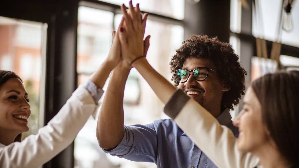 Diverse group of professionals high-fiving in a bright office space, celebrating teamwork, collaboration, and success.