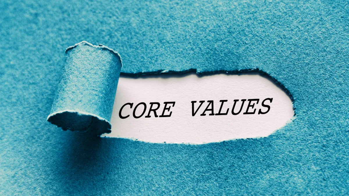 Torn blue paper revealing the words 'Core Values' underneath, symbolising integrity, purpose, and organisational principles.