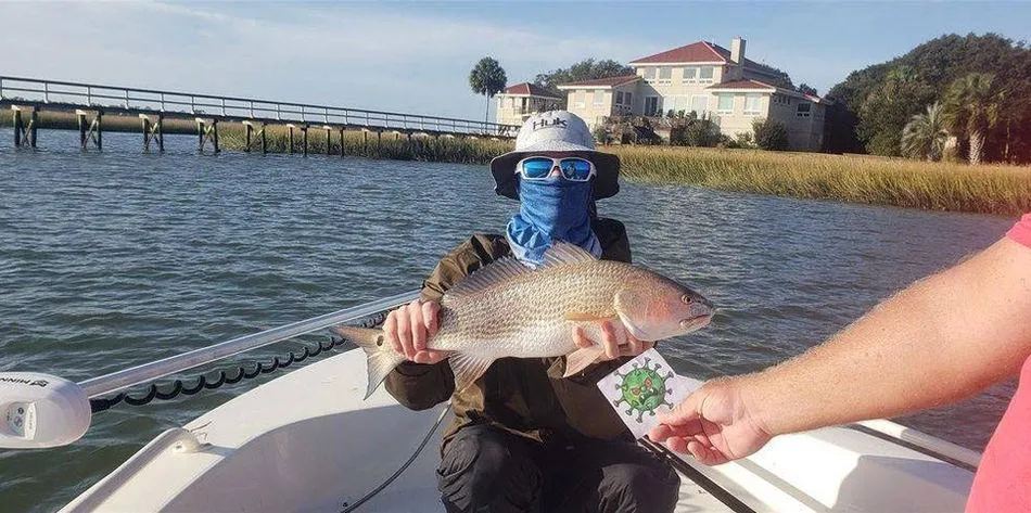 Angler wearing shades and face covering holding up his catch on a boat in Folly Beach, SC