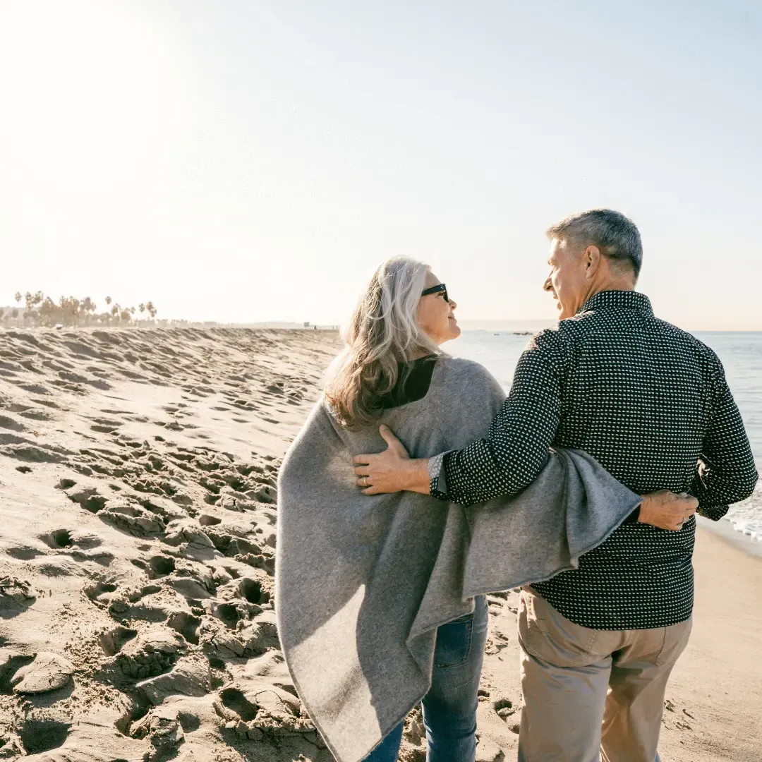 Elderly couple standing on the beach, gazing at each other with smiles