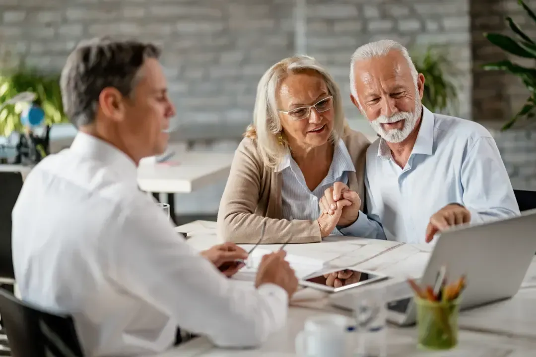 Elderly couple sitting and smiling at a laptop while consulting with an advisor