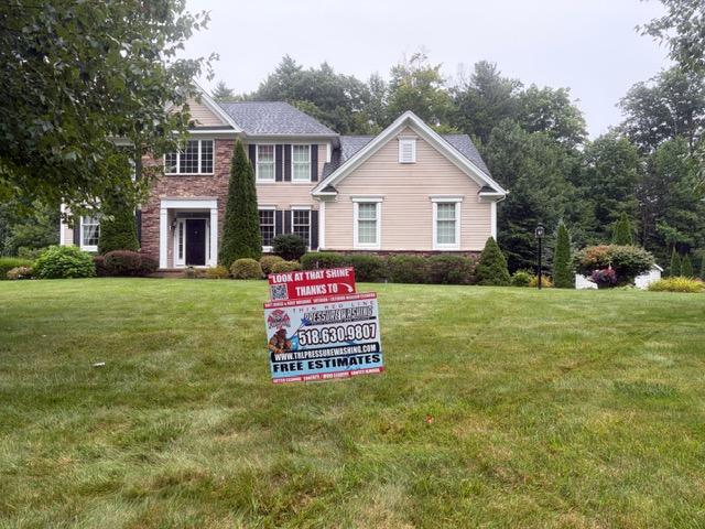 Residential house exterior cleaned by Thin Red Line Pressure Washing in Clifton Park, NY, with company service sign displayed on the lawn.