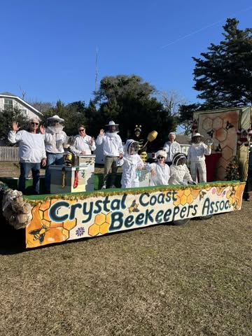 Portrait of Dr. Elena Morales, a Latina entomologist in her 40s, smiling warmly in a sunlit botanical garden, wearing a green field jacket and holding a notebook. The background features blooming wildflowers and bee boxes, emphasizing her expertise in pollinator research and community education.