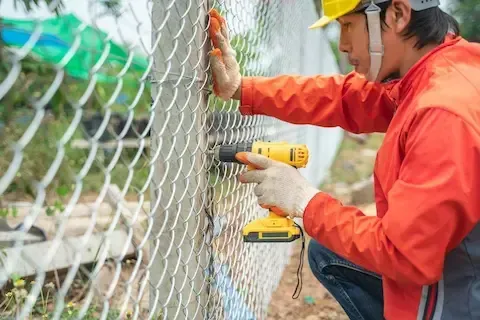 Professional fence contractor installing galvanized chain link fencing around a property