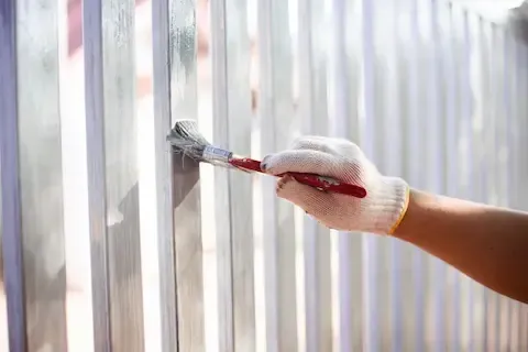 Gloved hand brushing white paint onto a wooden fence during a residential fence repair