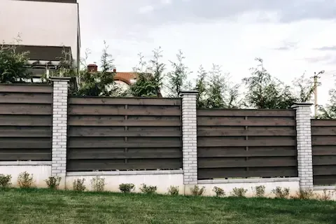 Modern horizontal wood fence with whitewashed brick columns bordering a landscaped garden